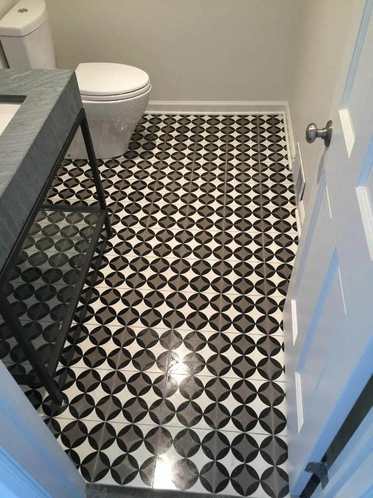 Powder room floor tile installation featuring black and white geometric patterned tiles with precise alignment