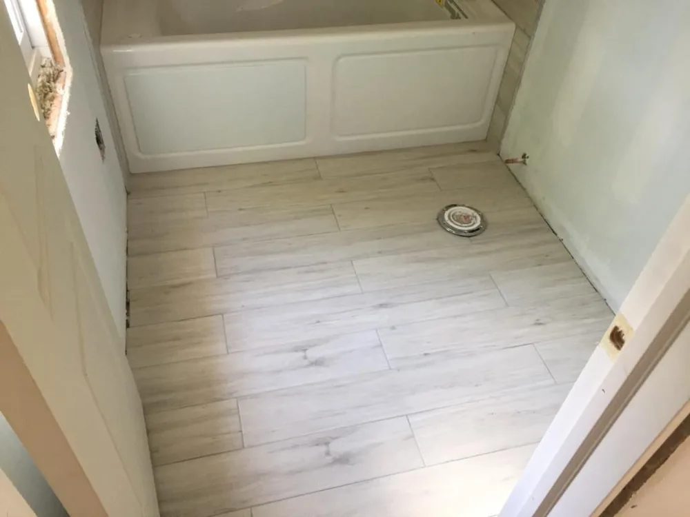 Bathroom floor tile installation with wood-look porcelain tiles and centered drain placement