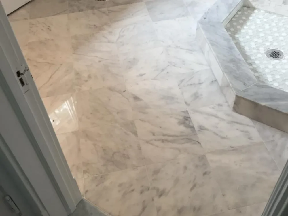 Close-up perspective of a bathroom marble floor installation, highlighting the polished natural stone finish and the step-in shower transition.