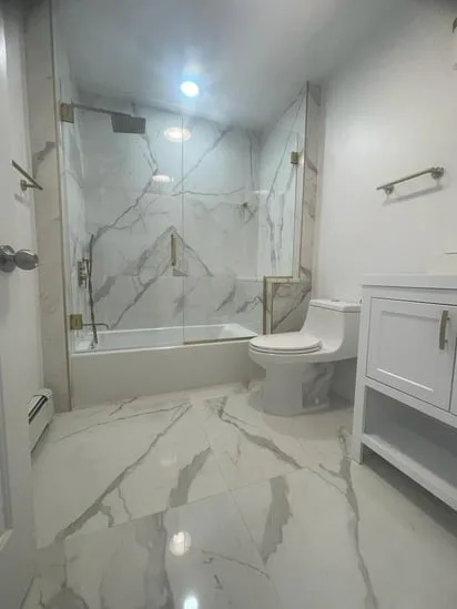 Finished bathroom remodel: Low-angle view looking into the luxurious glass shower with brass fixtures, a hand-held shower, and a built-in marble-tiled bench.