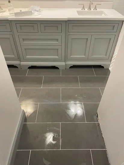 Large format gray floor tiles leading to a gray double vanity in a recent bathroom tile installation.