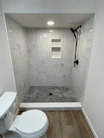 A detailed shot focusing on the back wall of a custom shower installation featuring a dual recessed shelf niche and white marble-veined tiling.