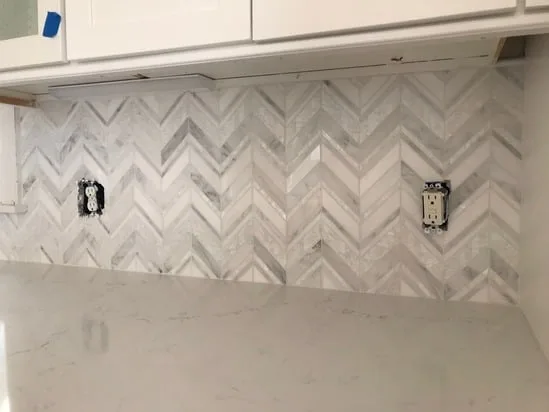 Detail shot of a chevron tile backsplash installation highlighting the symmetry and under-cabinet lighting integration.