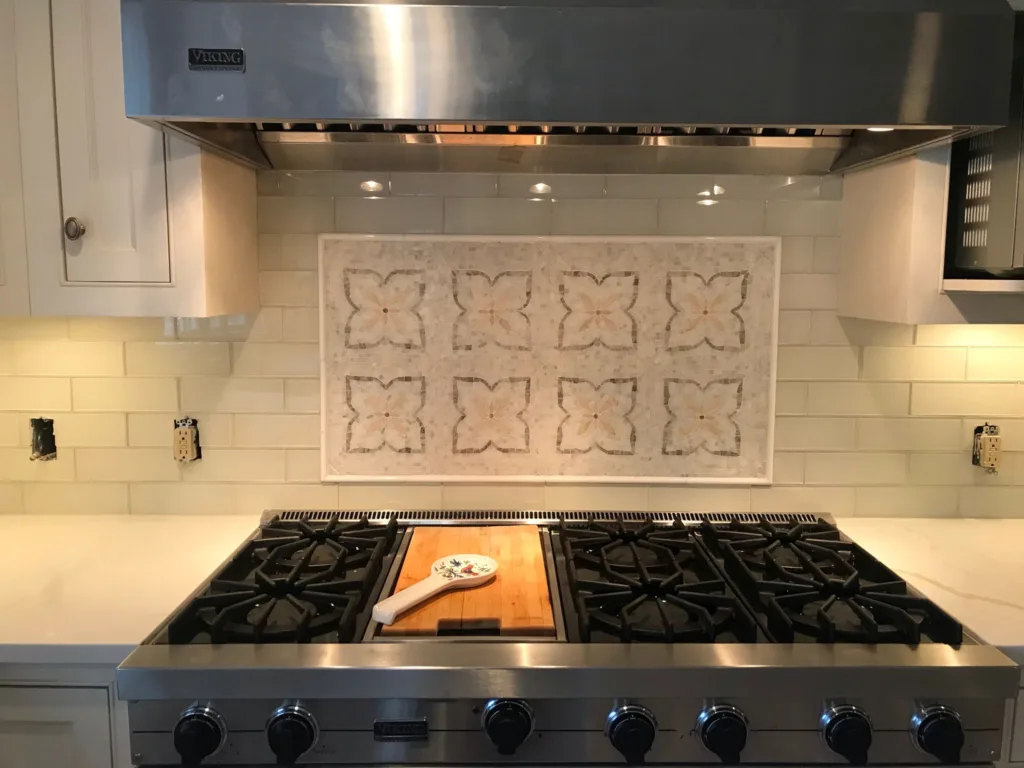 Kitchen backsplash tile installation featuring subway tiles and a decorative mosaic centerpiece behind a gas stove.