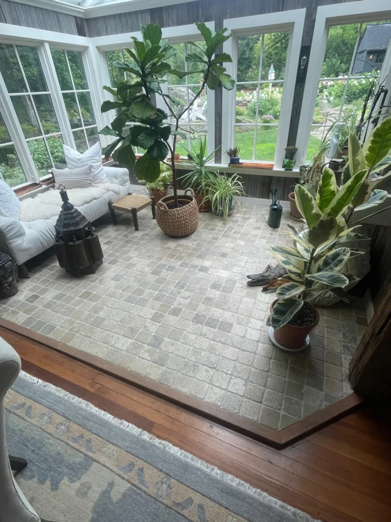 The completed and modern sunroom, featuring the newly installed light gray stone paver sunroom floor surrounded by plants and furniture.