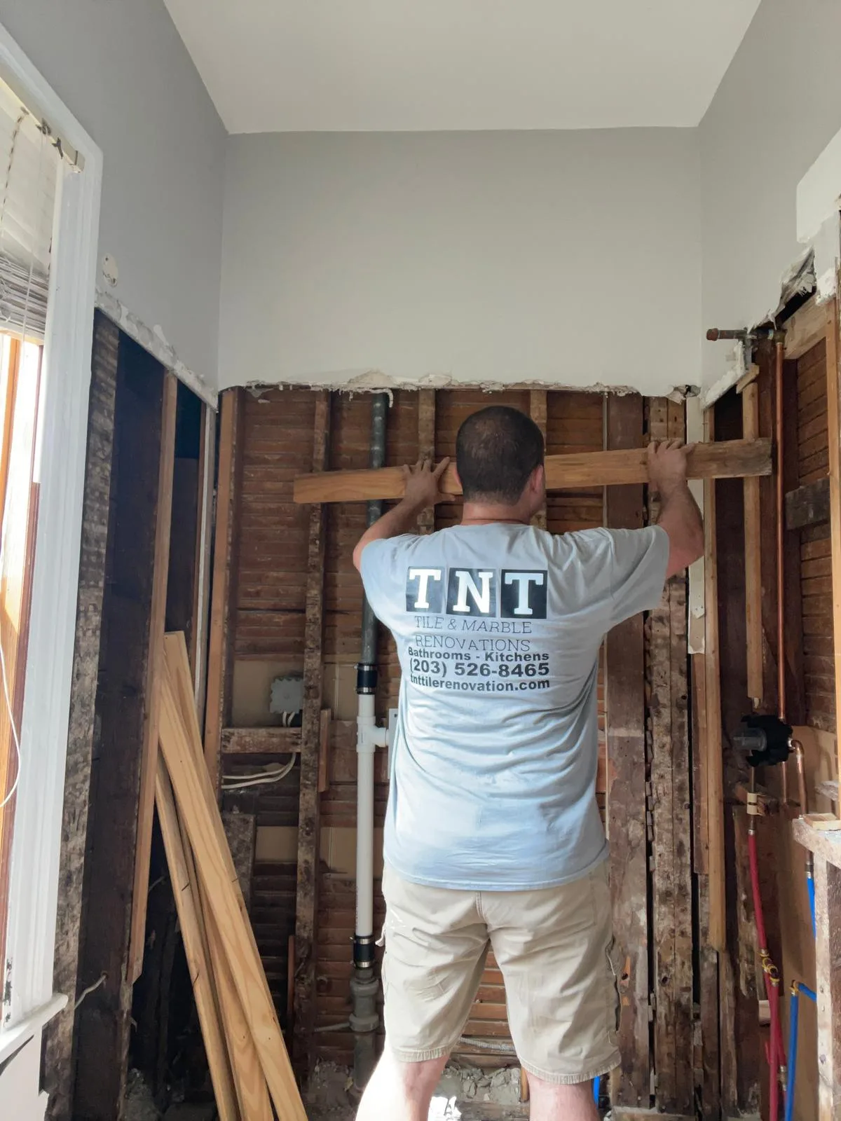 A contractor performing bathroom framing and plumbing reinforcements on an exposed stud wall.