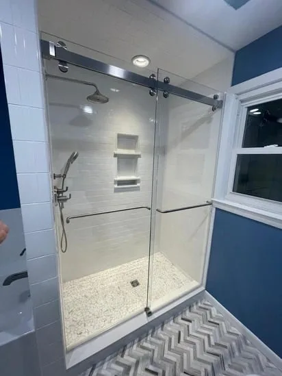 Frameless sliding glass shower enclosure with modern hardware from a blue bathroom remodel.